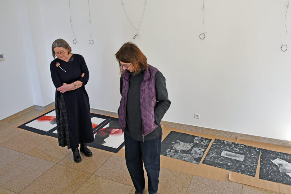 Jurorzy Triennale Litografii: dwóch mężczyzn i dwie kobiety chodzą po galerii BWA i oglądają porozkładane na podłodze prace na papierze.
